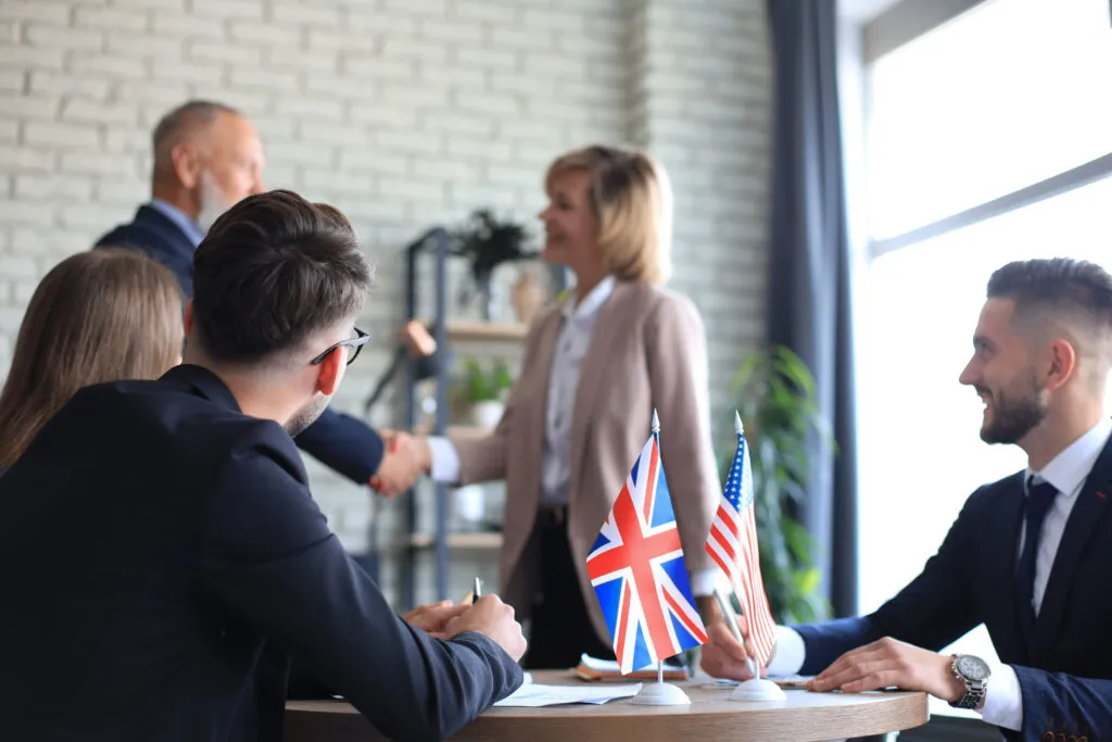 Capacitación en inglés empresarial para equipos de trabajo en una mesa de negociación con banderas internacionales.